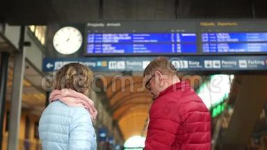 一对中年男女正在火车站台上等火车.. 看看<strong>日程安排表</strong>